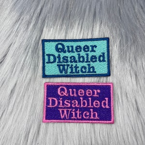 Puede incluir: Dos parches bordados con el texto "Queer Disabled Witch" en diferentes colores. El parche superior es turquesa con letras azul marino. El parche inferior es morado con letras rosas.