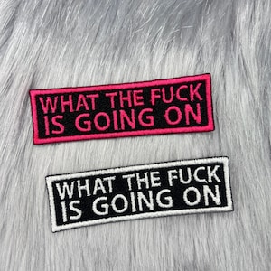 May include: Two black fabric patches with white and pink stitching. The patches read "What the fuck is going on".