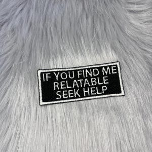 May include: A rectangular black embroidered patch with a white border and white stitched text that reads IF YOU FIND ME RELATABLE SEEK HELP. The patch features a clean, bold font and a durable fabric construction, designed for attachment to clothing.