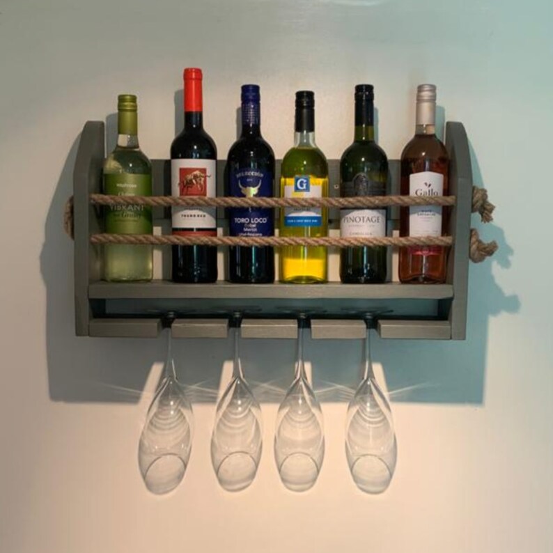 May include: A gray wooden wall-mounted wine rack with six bottles of wine and six wine glasses hanging below. The rack is decorated with rope and has a rustic look.