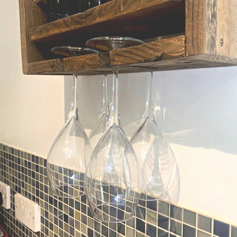 May include: A wooden wine rack with a shelf and hanging glass holders. The rack is mounted on a wall and has a rustic brown finish.