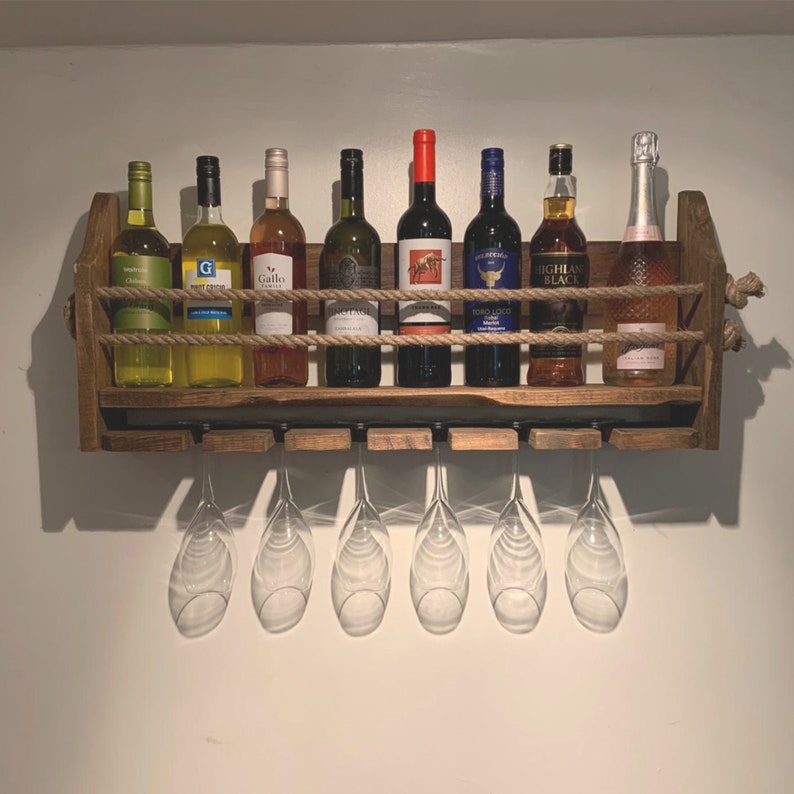 May include: A rustic wooden wine rack with rope accents holds eight bottles of wine and six wine glasses. The rack is mounted on a white wall.