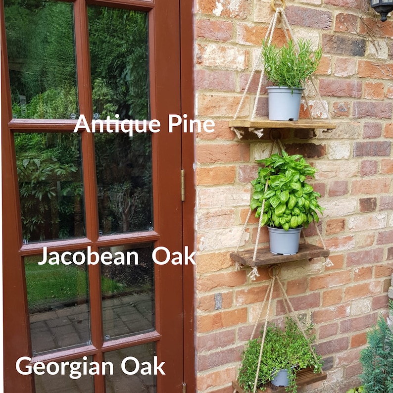 May include: Three hanging wooden shelves with plants in pots. The shelves are made of rustic wood and are hanging from the ceiling with rope. The plants are a variety of herbs, including rosemary, basil, and thyme. The shelves are labeled with the paint colors "Antique Pine", "Jacobean Oak", and "Georgian Oak".