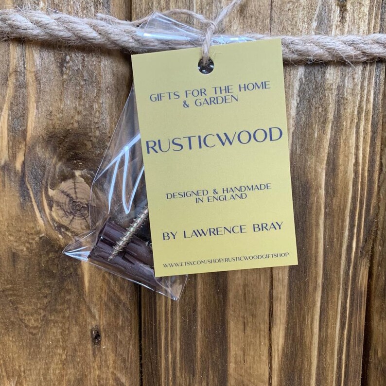 May include: A gold tag with the text "Gifts for the Home & Garden Rusticwood Designed & Handmade in England By Lawrence Bray www.etsy.com/shop/rusticwoodgiftshop" on a wooden background.