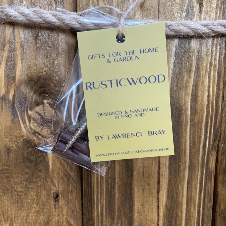 May include: A gold tag with the text "Gifts for the Home & Garden Rusticwood Designed & Handmade in England By Lawrence Bray www.etsy.com/shop/rusticwoodgiftshop" on a wooden background.