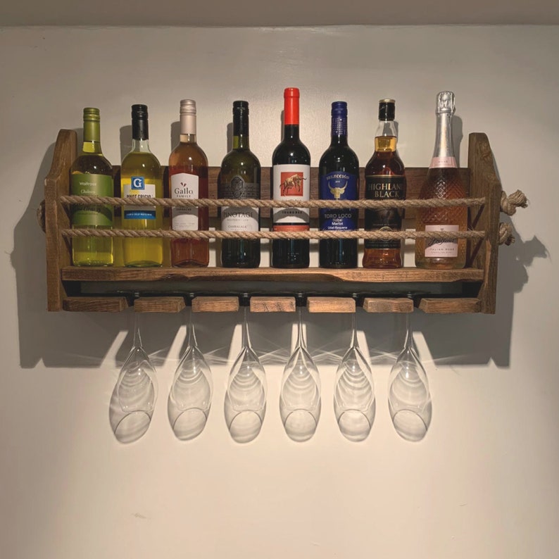 May include: A wooden wine rack with a rope design, holding eight bottles of wine and six wine glasses. The rack is mounted on a white wall.