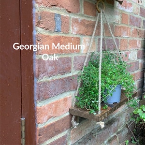 May include: A wooden hanging shelf with a plant in a gray pot. The shelf is made of oak and has a rope hanging system. The text "Georgian Medium Oak" is visible on the shelf.