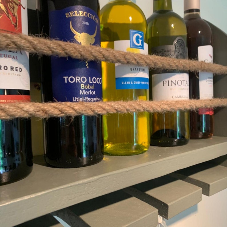 May include: A wooden wine rack with five bottles of wine. The rack is painted a light gray color and has a rope wrapped around it. The bottles are a mix of red and white wine. The labels on the bottles are visible. The text on the labels reads "SELECCI&Oacute;N 2018", "TORO LOCO Bobal Merlot Utiel-Requena", "GRAPEVINE CLEAN & CRISP WHITE WINE", "PINOTA CAMBALA", and "GARNIER".