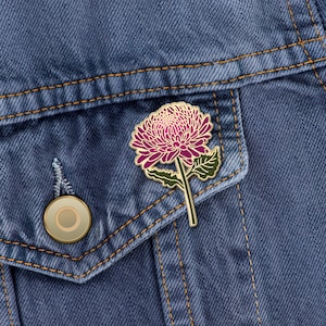 以下が含まれることがあります： デニムジャケットにつけられた、紫と緑のエナメル製の菊の花のピン