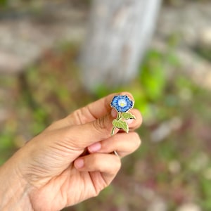 May include: Gold-tone enamel pin featuring a blue morning glory flower with a white center and green leaves.