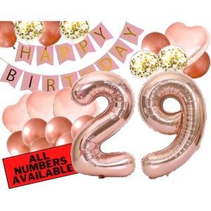 May include: Rose gold number balloons for a 29th birthday party. The balloons are surrounded by smaller rose gold balloons, confetti balloons, and a pink banner that says "Happy Birthday".