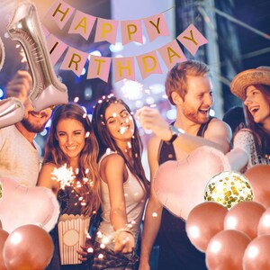 May include: A group of friends celebrating a 21st birthday with rose gold balloons, confetti balloons, and a pink banner that says "Happy Birthday".