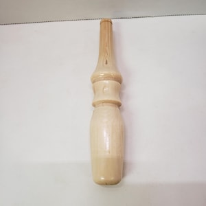 Puede incluir: Un enhebrador de lana de madera con un acabado liso de color marrón claro. El enhebrador tiene una forma redondeada y bulbosa con un cuello estrecho.