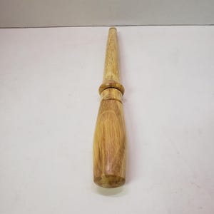 Puede incluir: Un mazo de madera de color marrón claro con una cabeza redonda. El mazo tiene un acabado liso y pulido.
