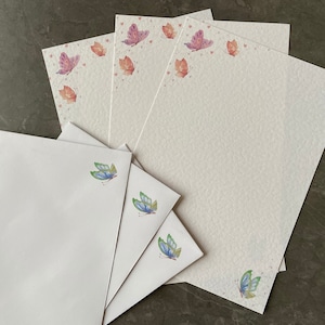 May include: Set of white stationery paper with a delicate butterfly design. The paper features a subtle watercolour effect and is perfect for writing letters or notes.
