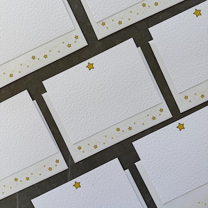 May include: A set of white note cards with a gold star design. The cards have a textured surface and are perfect for writing notes or sending greetings.
