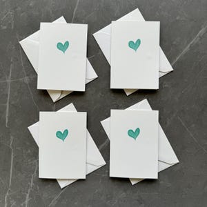 May include: Four white blank greeting cards with teal heart designs. The cards are folded in half and have white envelopes.