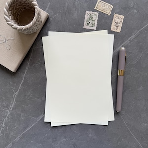 May include: A blank white sheet of paper with a pen on a gray marble surface. There are three vintage postage stamps on the surface.