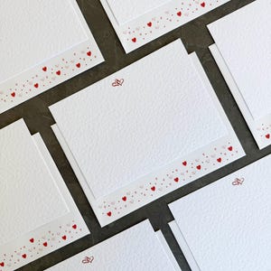 May include: Set of white note cards with a red heart border and a red heart design in the centre. The cards are ideal for writing notes or sending greetings.