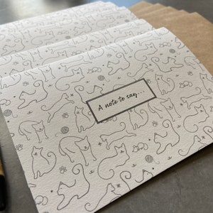 May include: A white card with a black and white pattern of cats. The card has a black rectangle with the text "A note to say..." in white.