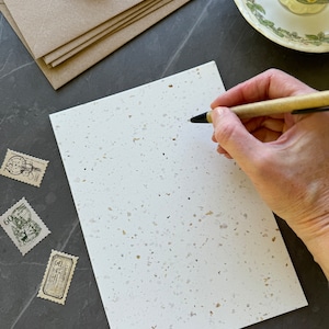 Puede incluir: Una tarjeta blanca con textura moteada, un bol&iacute;grafo y varios sellos postales antiguos. La tarjeta est&aacute; en blanco y lista para escribir.
