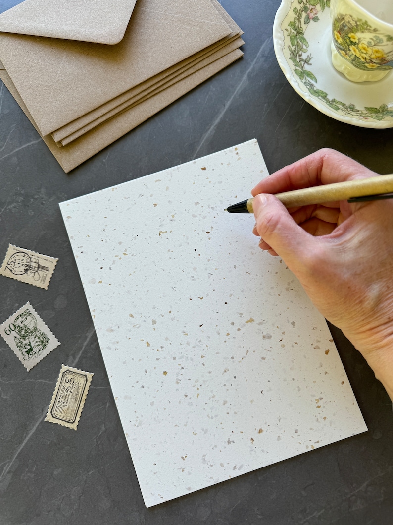 Puede incluir: Una tarjeta blanca con textura moteada, un bol&iacute;grafo y varios sellos postales antiguos. La tarjeta est&aacute; en blanco y lista para escribir.