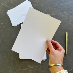 May include: A white sheet of paper with a textured surface is being held by a hand. The paper is blank and ready for writing or drawing.