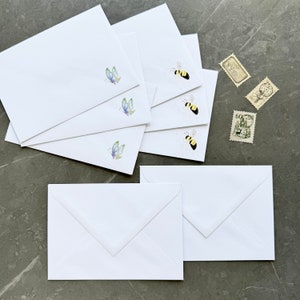 May include: A set of six white envelopes with different designs. The envelopes feature butterflies and bees in watercolour illustrations.