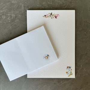May include: A set of two blank white stationery cards with floral designs. The larger card has a floral border at the top and a single daisy with a ladybug in the bottom right corner. The smaller card has a single daisy with a ladybug in the bottom right corner.