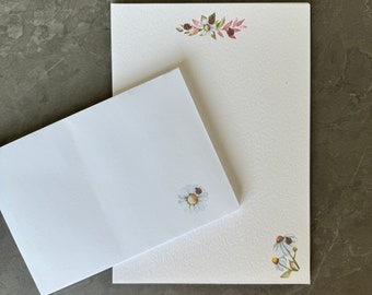 May include: A set of two blank white stationery cards with floral designs. The larger card has a floral border at the top and a single daisy with a ladybug in the bottom right corner. The smaller card has a single daisy with a ladybug in the bottom right corner.