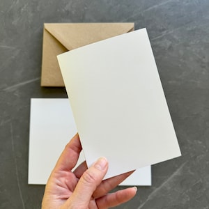 May include: A blank white card held in a hand, with a brown envelope behind it.