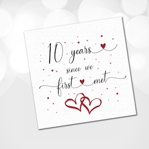 May include: A white card with the text "10 years since we first met" in black cursive writing. The card is decorated with small red hearts.