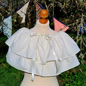 May include: A white, double-layered, ruffled collar with a satin ribbon tied in a bow at the center.