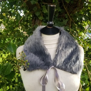May include: A gray faux fur collar with a silver satin ribbon tie. The collar is displayed on a white mannequin.