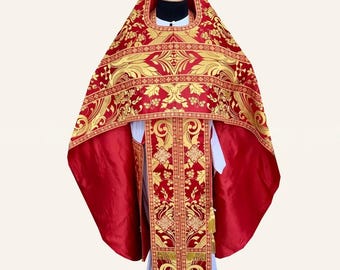 May include: A red and gold liturgical vestment featuring intricate metallic embroidery with floral and cross motifs. The garment includes a wide, draped cape section and a long, rectangular front panel adorned with gold fringe at the hem.