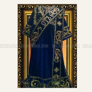 Pode incluir: Uma casula litúrgica de veludo azul com bordados dourados. A casula apresenta um padrão decorativo de motivos florais estilizados e uma cruz. O texto "IC XC NIKA" está bordado na casula.
