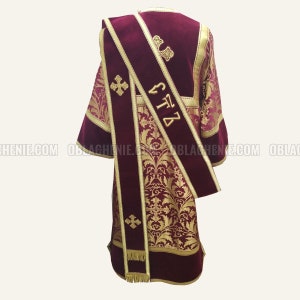 Pode incluir: Uma veste litúrgica bordô com bordados dourados e uma estola combinando em bordô com detalhes dourados. A estola tem uma cruz dourada e a inscrição "S.T.Z." bordada.
