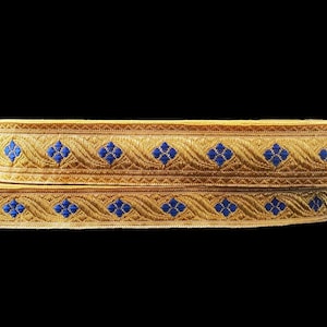 Puede incluir: Dos cintas de adorno doradas con un patrón de diamante azul. El adorno está tejido con un hilo de oro texturizado.
