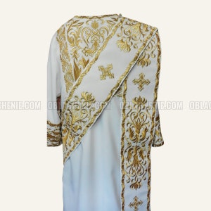 Pode incluir: Vestuário litúrgico branco com bordado dourado. O vestuário apresenta um padrão decorativo com motivos florais e cruzes.