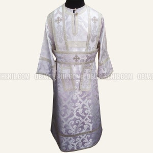 May include: White liturgical vestment with silver embroidery and a floral pattern. The vestment has a high collar and long sleeves.