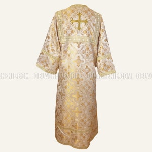 May include: A white liturgical vestment with gold embroidery. The vestment features a cross design and a floral pattern.