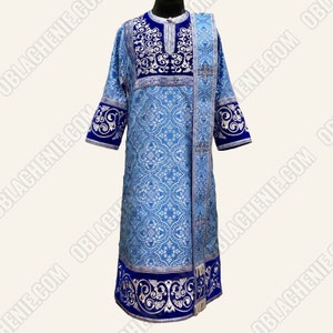Pode incluir: Uma veste litúrgica azul e prateada com um desenho bordado azul e prateado. A veste tem uma forma longa e fluida e uma gola larga e decorativa.