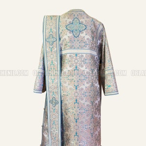 Pode incluir: Uma veste litúrgica branca e azul com um padrão de cruz e bordados ornamentados. A veste tem um design longo e fluido e é feita de um tecido luxuoso.