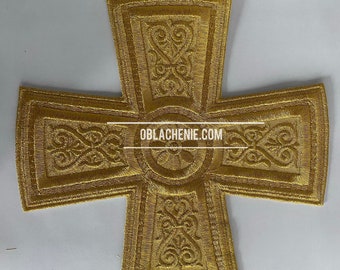 May include: A gold embroidered cross with intricate designs. The cross is made of fabric and has a raised, textured surface. The text "OBLACHENIE.COM" is printed in the center of the cross.