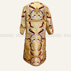 Pode incluir: Uma veste litúrgica dourada e bordô com bordados intrincados e um desenho de cruz. A veste tem uma silhueta longa e fluida e é adornada com uma variedade de elementos decorativos.