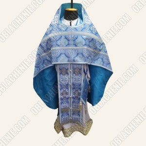 May include: A blue and silver liturgical vestment with intricate patterns and a white undergarment. The vestment has a decorative cross on the front and a matching stole.