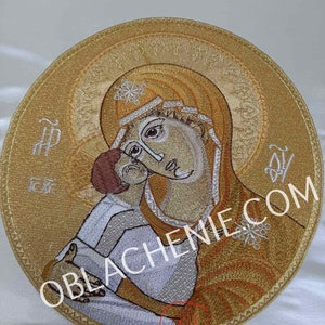 Puede incluir: Icono bordado de la Virgen María y el niño Jesús en un marco circular. El icono está sobre un fondo blanco y presenta un bordado de hilo dorado y blanco.