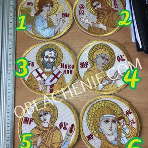 May include: Six embroidered round patches with religious imagery. Each patch features a different saint or religious figure, including an angel, a man with a beard, and a woman with a child. The patches are all white with gold embroidery and have a red border.