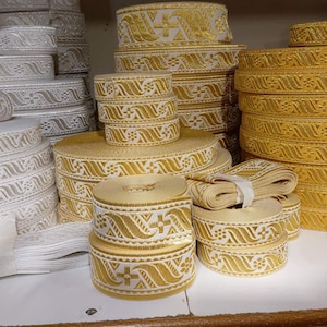 Puede incluir: Una variedad de cintas decorativas en blanco, dorado y rojo. Las cintas están enrolladas y apiladas, mostrando patrones detallados. Ideal para manualidades y adornos. Medidas en centímetros.