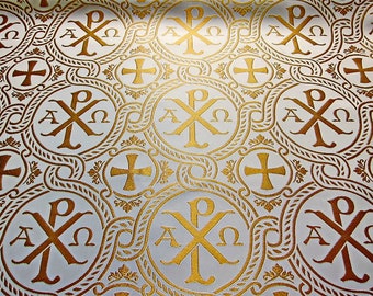 Op de afbeelding: Witte stof met een herhalend patroon van gouden cirkels met de Griekse letters Alpha, Chi en Omega, en een kruis. Het patroon is omgeven door een gouden touwontwerp.